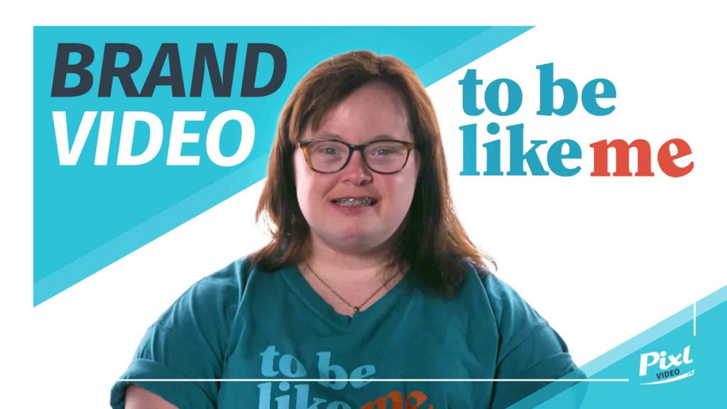 young lady with down's syndrome looking directly into the camera for an interview, wearing t-shirt reading "to be like me"